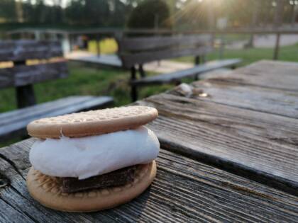 Vaahtokarkki keksien välissä pöydällä, taustalla kesäinen ranta.