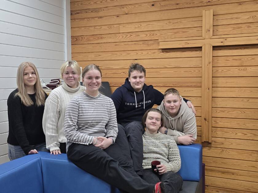 Kuusi nuorta sohvalla, taustalla seinän kokoinen risti