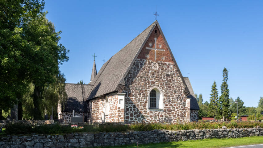 Keskiaikainen kivi kirkko kesäisellä ilmalla, taustalla sininen pilveetön taivas, edessä asfalttitietä
