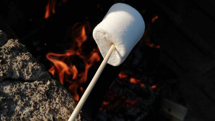 Grillitikku nojaa kivireunaan ja siinä on vaalea vaahtokarkki, alapuolella varjoissa liekki.